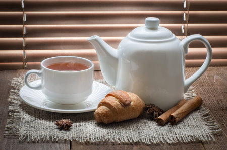 tea cup with teapot on old wooden table against the background of blindsの写真素材