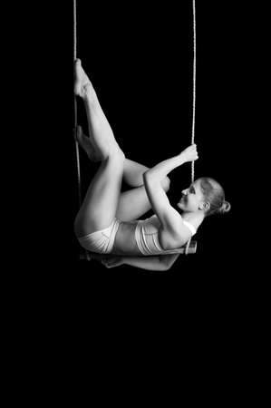 Young woman gymnast on a trapeze over black background の写真素材
