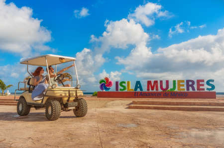 Smiling and happy couple driving a golf cart at tropical beach on Isla Mujeres, Mexicoの写真素材