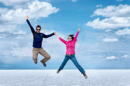 Happy couple jumping in Uyuni Salt Flats against cloudy sky, Bolivia, South Americaの写真素材