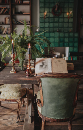 Composition of candlesticks, houseplants and books on the vintage table in blurred interior