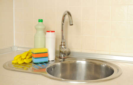 Detergent bottles and sponges near the faucet in the kitchenの写真素材