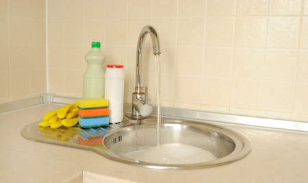 Detergent bottles and sponges near the faucet in the kitchenの写真素材