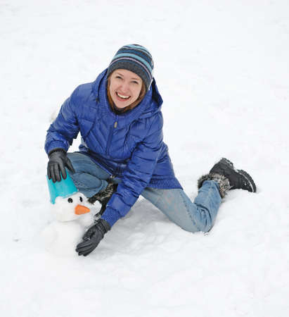 Smiling woman sculpts snowman with blue bucketの写真素材
