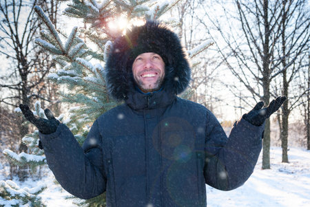 Smiling man wearing fur hooded parka coat in the winter park
