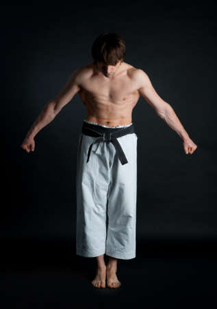 Man in a kimono with a black belt bows on black backgroundの写真素材