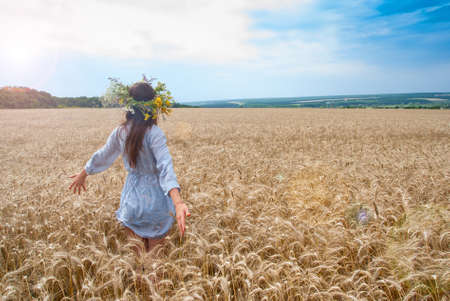 Beautiful girl in  wreath in the field of ripe wheat with lens flare effectの写真素材