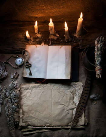 Magic fairytale table in the hut with window to the garden with open ancient book and burning candlesの写真素材