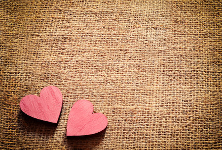 Two red wooden hearts on sackcloth, canvas background. Vintage style.