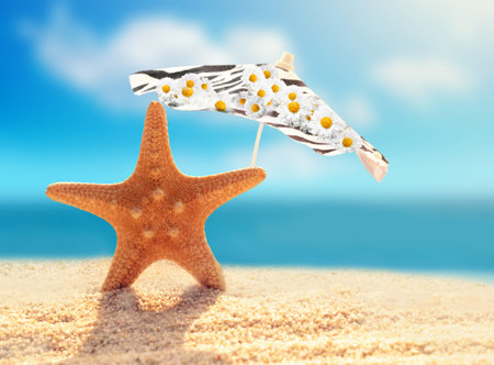 Summer beach.  Starfish and umbrella on a beach sand against the background of the ocean.の写真素材