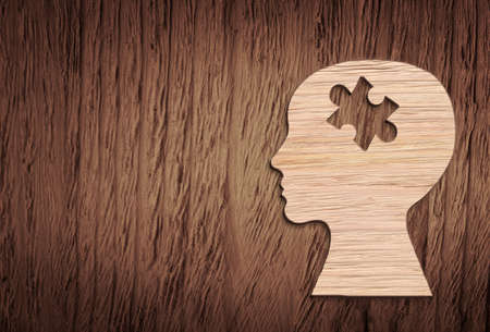 Human head silhouette with a jigsaw piece cut out on the wooden background, mental health symbolの写真素材