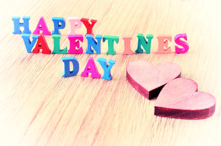 The words happy valentines day made with block wooden letters next to couple of hearts on light wooden backgroundの写真素材