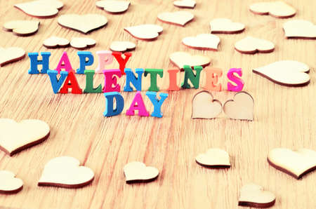 The words happy valentines day made with block wooden letters next to couple of hearts on light wooden backgroundの写真素材