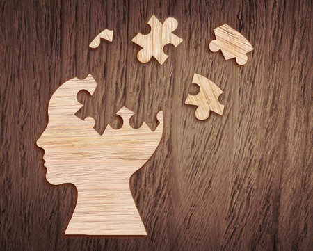 Human head silhouette with a jigsaw piece cut out on the wooden background, mental health symbolの写真素材