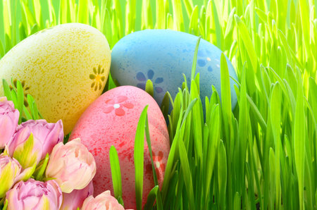 Painted Easter eggs, pink flowers in a bucket in green grass.