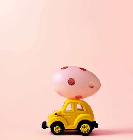 Easter egg and toy car on pink background, happy easter day concept.の写真素材