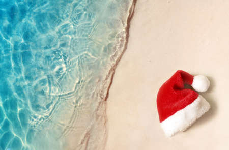 Christmas holidays concept. Top view of santa claus hat on summer sand beachの写真素材