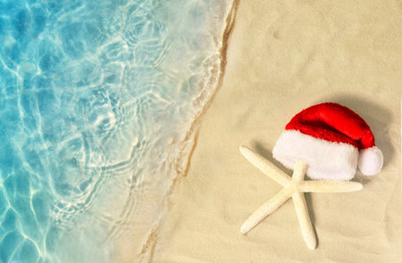 Christmas holidays concept. Top view of starfish in santa claus hat on summer sand beach