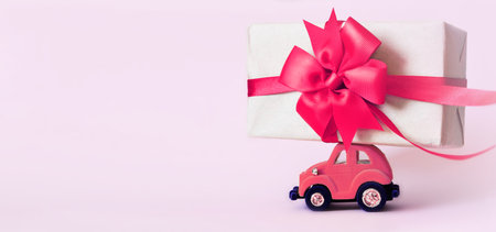 Pink toy retro car with gift box on a roof on pink background. Copy spaceの写真素材