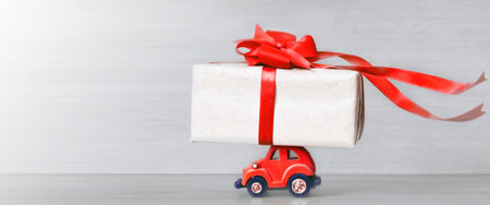 Red toy retro car with gift box on a roof on gray background. Copy spaceの写真素材
