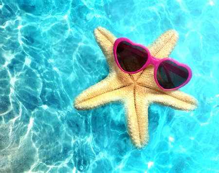 Starfish in sunglasses on the summer beach in sea water. summer background. summertime.の写真素材