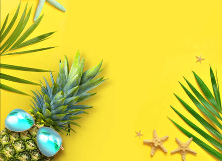 Summer background design concept. Top view of holiday travel beach with starfish, pineapple and palm leaves on yellow background.の写真素材