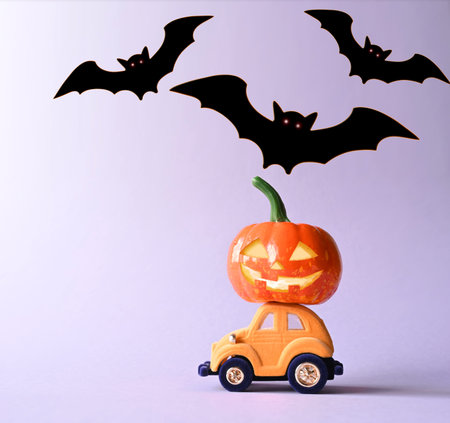 Toy car with funny pumpkin on the roof and bats on purple background. Space for text. Halloween...