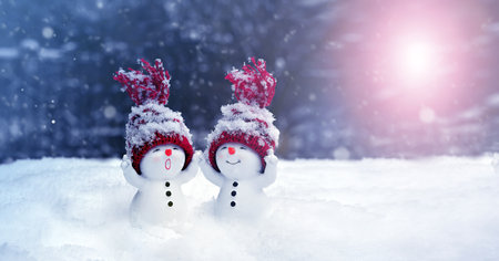 Two little snowmen in caps on snow in the winter. Festive background with a funny snowman. Christmas card, copy space.の写真素材