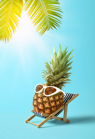 Pineapple in sunglasses relaxes on lounge chair on beach. Summer tropical minimal humor concept.の写真素材