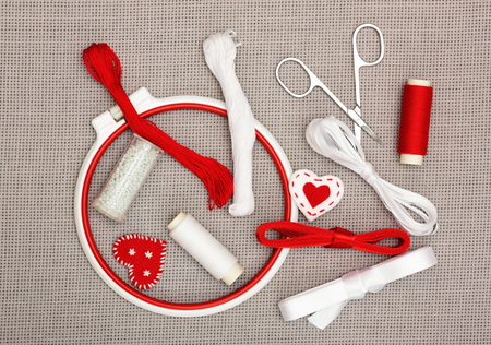 The embroidery hoop, red and white sewing threads, ribbons, beads on canvas backgroundの写真素材