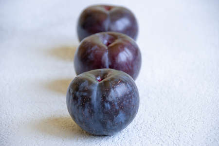 a row of three blue plums on a gray concrete backgroundの写真素材