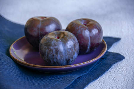 three blue plums on a purple plate on a blue napkinの写真素材
