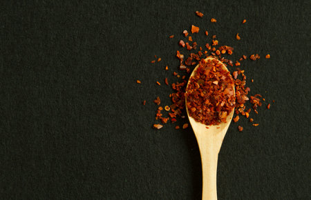 Spoon with red pepper on the black background with copy space