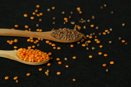 Two wood spoon with lentil and buckwheat on black background