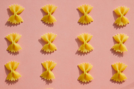 MaÑaroni or pasta bow shape in row on pink background