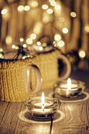 Ceramic stylish cups in sweaters and christmas retro garland on bokeh lights background. Shallow depth of field. Tinted photo.の写真素材