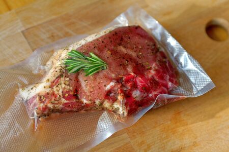 Close up of a vacuum-packed pork steak on a wooden cutting board.の写真素材