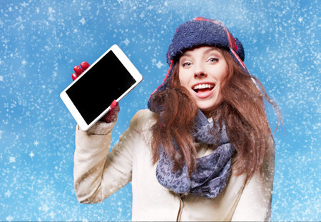 christmas, x-mas, electronics, gadget concept - smiling woman in winter clothes with tablet pc on blue background