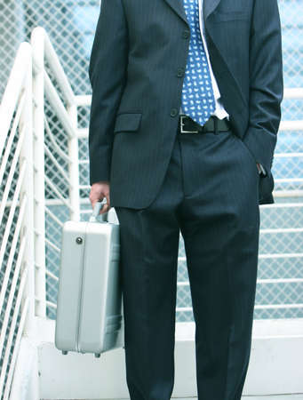business man holds onto his briefcase while standing on the stairsの写真素材