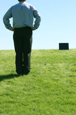 Business man standing near his laptop on a grassy hillの写真素材