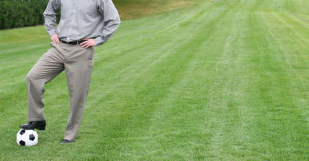 Business man stands on top of a soccer ball in a parkの写真素材
