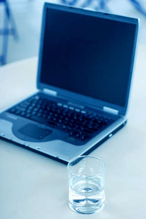 Business laptop sits on the table next to a glass of waterの写真素材