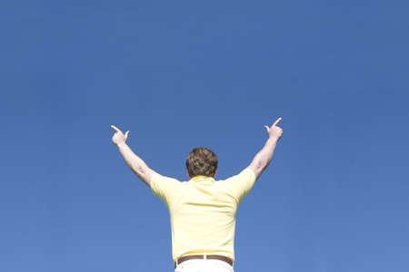 Man raises arms and points with his fingers under a blue skyの写真素材