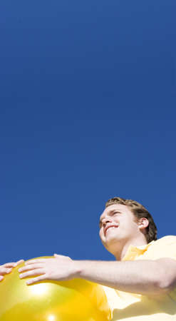 Happy Man holds a big, yellow ball and looks off to the distance under a blue skyの写真素材