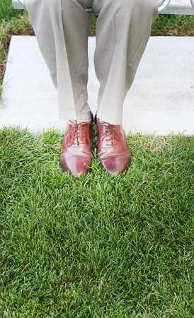 Business man's shoes in the green grass as he is sitting on the benchの写真素材