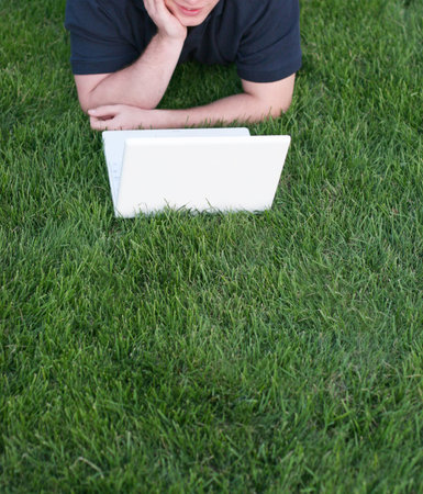 Business man is relaxing as he is looking at his white laptop in the green grassの写真素材