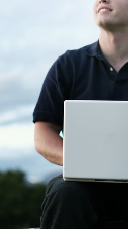 Business man in blue, casual shirt is typing on his white laptop as he is looking up to the sky