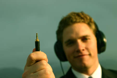 Business man is wearing incredibly large set of headphones and is holding the plug-in piece in front of youの写真素材