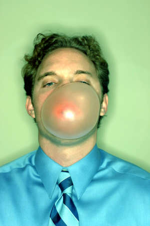 Business man wearing blue shirt and blue tie is blowing a big bubble with his bubble gumの写真素材