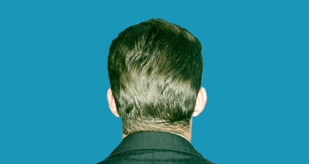 Back of business man's head with a full head of hair; he is wearing a gray suit against a light blue backgroundの写真素材